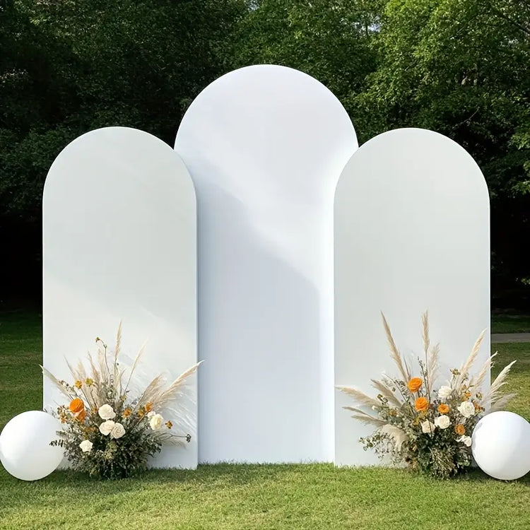 White archway with floral arrangements and balloons on a grassy area
